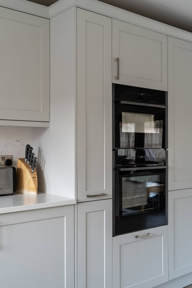Inspiration for a mid-sized traditional separate kitchen in Oxfordshire with a single-bowl sink, recessed-panel cabinets, grey cabinets, quartzite benchtops, black appliances, grey floor and white benchtop.