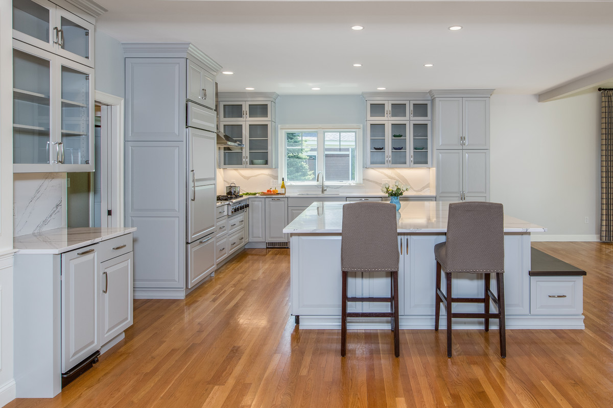 Large transitional l-shaped medium tone wood floor open concept kitchen photo in Boston with an undermount sink, raised-panel cabinets, gray cabinets, quartz countertops, stone slab backsplash, paneled appliances and an island