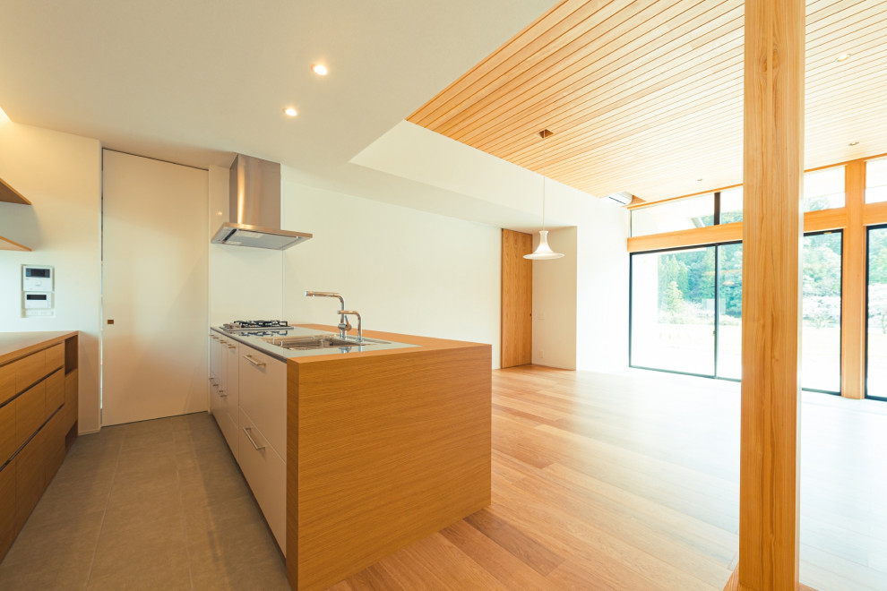 Idéer för ett grå linjärt kök med öppen planlösning, med skåp i mellenmörkt trä, bänkskiva i rostfritt stål, vitt stänkskydd, stänkskydd i cementkakel, rostfria vitvaror, mellanmörkt trägolv, en halv köksö och brunt golv
