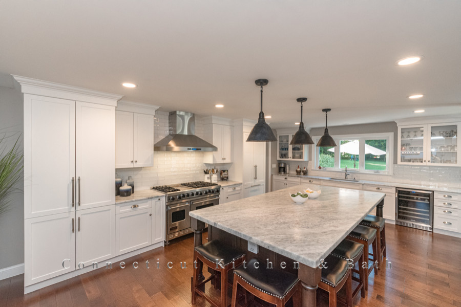 This is an example of an expansive transitional kitchen in New York with white splashback, stainless steel appliances, with island and multi-coloured benchtop.