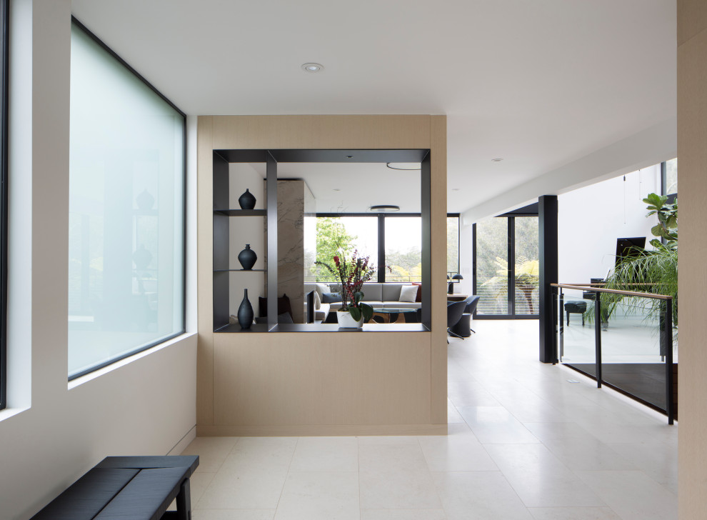 Cette image montre un hall d'entrée minimaliste de taille moyenne avec un mur blanc, un sol en calcaire, une porte simple, une porte en bois brun et un sol blanc.