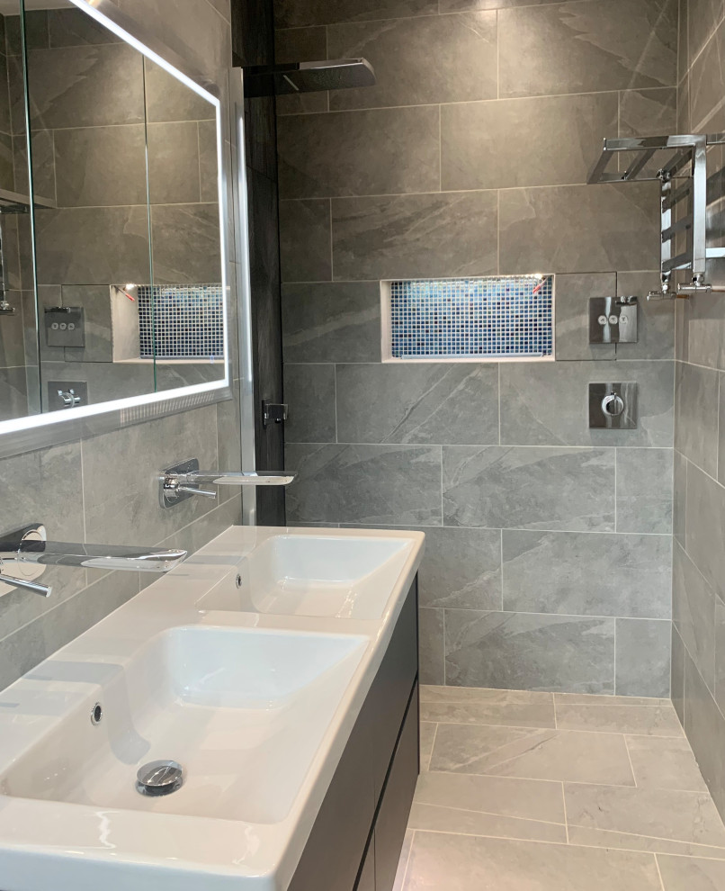 Foto på ett mellanstort en-suite badrum, med släta luckor, blå skåp, våtrum, en vägghängd toalettstol, grå kakel, porslinskakel, grå väggar, klinkergolv i porslin, ett väggmonterat handfat, grått golv och med dusch som är öppen