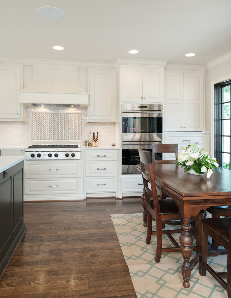 Large arts and crafts u-shaped eat-in kitchen in Kansas City with a farmhouse sink, raised-panel cabinets, white cabinets, quartz benchtops, white splashback, terra-cotta splashback, stainless steel appliances, dark hardwood floors and with island.