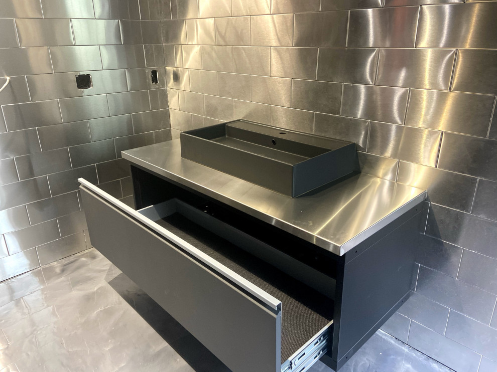 Design ideas for a contemporary cloakroom in New York with flat-panel cabinets, black cabinets, a one-piece toilet, grey tiles, metal tiles, grey walls, concrete flooring, a vessel sink, stainless steel worktops, grey floors, grey worktops and a floating vanity unit.