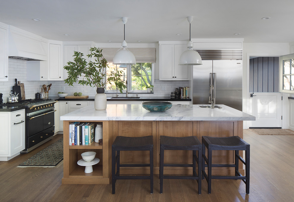 Design ideas for a mid-sized transitional l-shaped open plan kitchen in San Francisco with beaded inset cabinets, white cabinets, marble benchtops, white splashback, with island, brown floor, white benchtop, an undermount sink, cement tile splashback, stainless steel appliances and medium hardwood floors.
