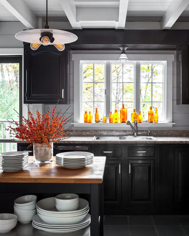 Photo of a country single-wall kitchen in New York with a drop-in sink, raised-panel cabinets, black cabinets, grey splashback, with island and black floor.