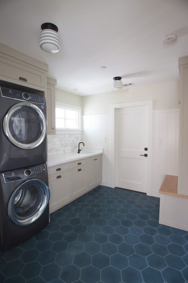 This is an example of a mid-sized country single-wall utility room in San Francisco with an undermount sink, shaker cabinets, grey cabinets, quartzite benchtops, white walls, concrete floors, a stacked washer and dryer, blue floor and white benchtop.