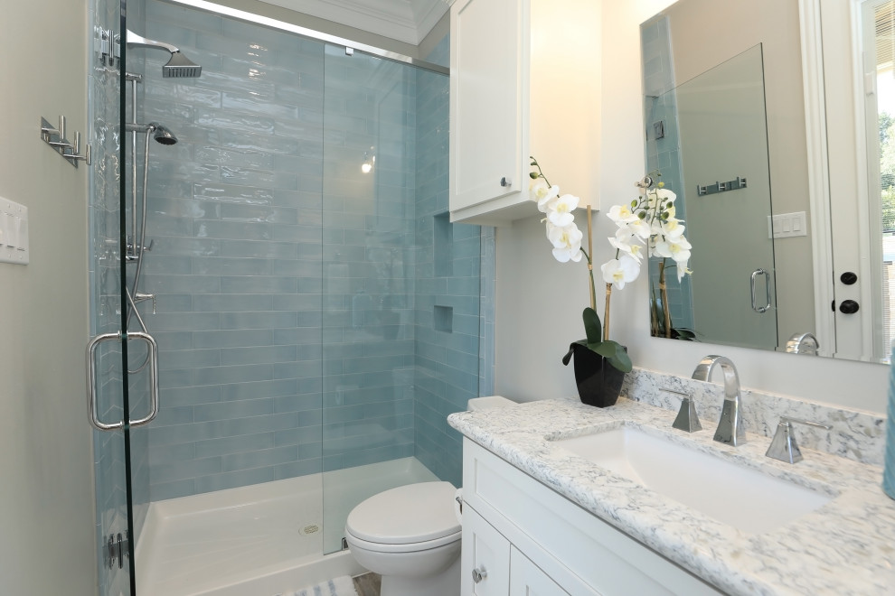 Photo of a small beach style bathroom in Houston with recessed-panel cabinets, white cabinets, an alcove shower, a two-piece toilet, blue tile, subway tile, white walls, vinyl floors, an undermount sink, granite benchtops, multi-coloured floor, a hinged shower door, white benchtops, a single vanity and a built-in vanity.