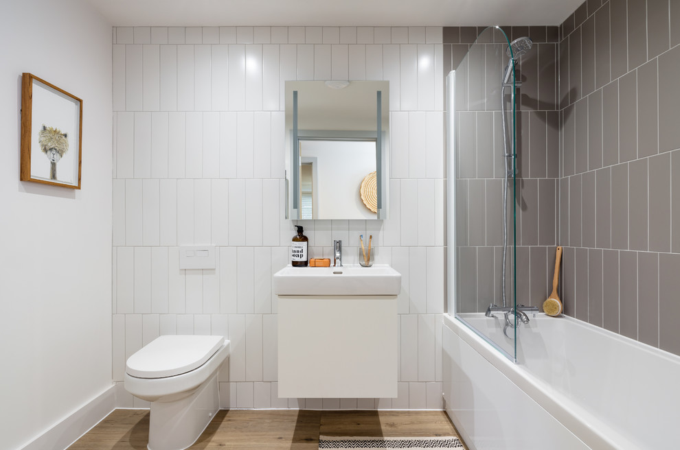 Inspiration for a modern bathroom in Dorset with flat-panel cabinets, white cabinets, a drop-in tub, a shower/bathtub combo, a one-piece toilet, gray tile, ceramic tile, white walls, laminate floors, a drop-in sink and a hinged shower door.