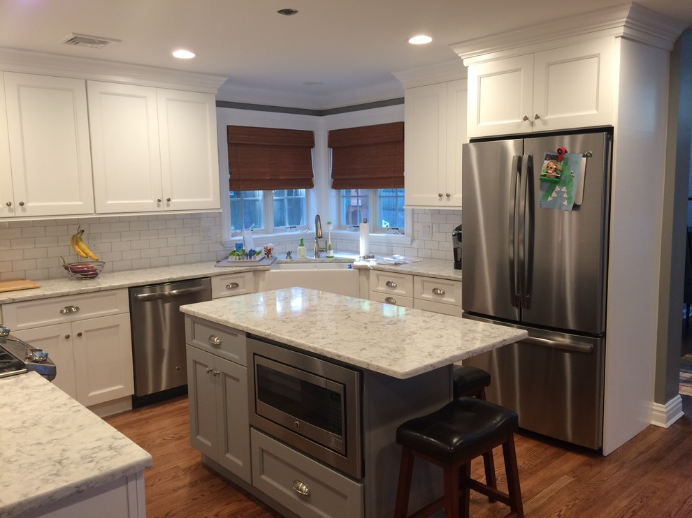 Eat-in kitchen - mid-sized transitional u-shaped light wood floor and brown floor eat-in kitchen idea in New York with a farmhouse sink, shaker cabinets, white cabinets, quartz countertops, white backsplash, porcelain backsplash and stainless steel appliances