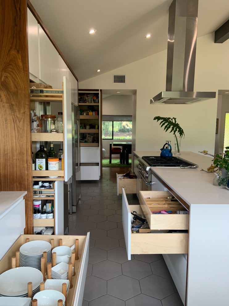 Photo of a mid-sized midcentury l-shaped open plan kitchen in San Diego with an undermount sink, flat-panel cabinets, white cabinets, quartz benchtops, white splashback, engineered quartz splashback, stainless steel appliances, porcelain floors, with island, grey floor, white benchtop and vaulted.