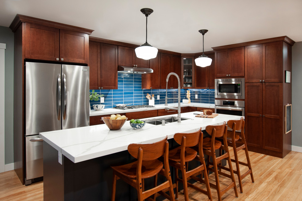 Design ideas for a large traditional l-shaped kitchen/diner in San Francisco with a double-bowl sink, shaker cabinets, brown cabinets, blue splashback, glass tiled splashback, stainless steel appliances, light hardwood flooring, an island, yellow floors and white worktops.