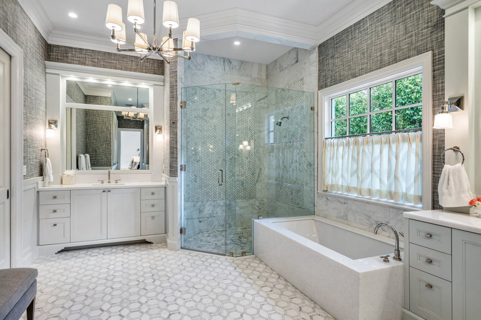 This is an example of a large classic ensuite wet room bathroom in Miami with recessed-panel cabinets, white cabinets, a submerged bath, grey tiles, marble tiles, grey walls, a submerged sink, grey floors, a hinged door, white worktops, a shower bench, double sinks, a built in vanity unit, wallpapered walls and a one-piece toilet.