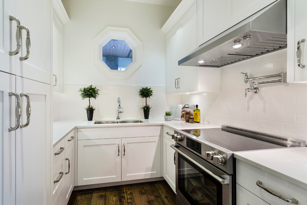 Enclosed kitchen - huge rustic l-shaped medium tone wood floor and brown floor enclosed kitchen idea in Vancouver with an undermount sink, shaker cabinets, white cabinets, solid surface countertops, white backsplash, ceramic backsplash, stainless steel appliances and white countertops