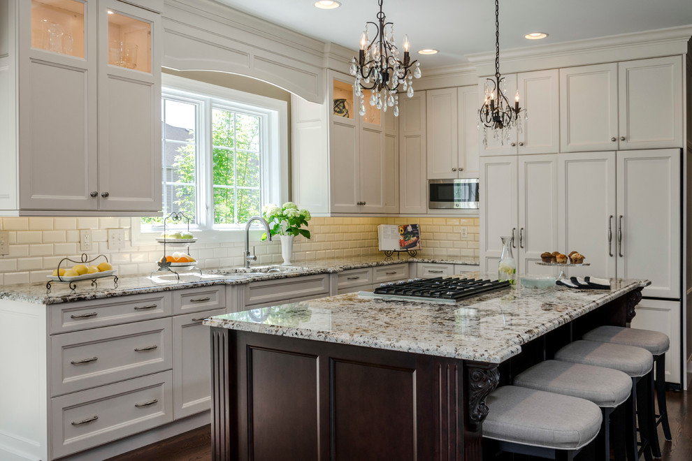 This is an example of a traditional l-shaped kitchen in Chicago with an undermount sink, beaded inset cabinets, white cabinets, white splashback, subway tile splashback, stainless steel appliances, dark hardwood floors and with island.