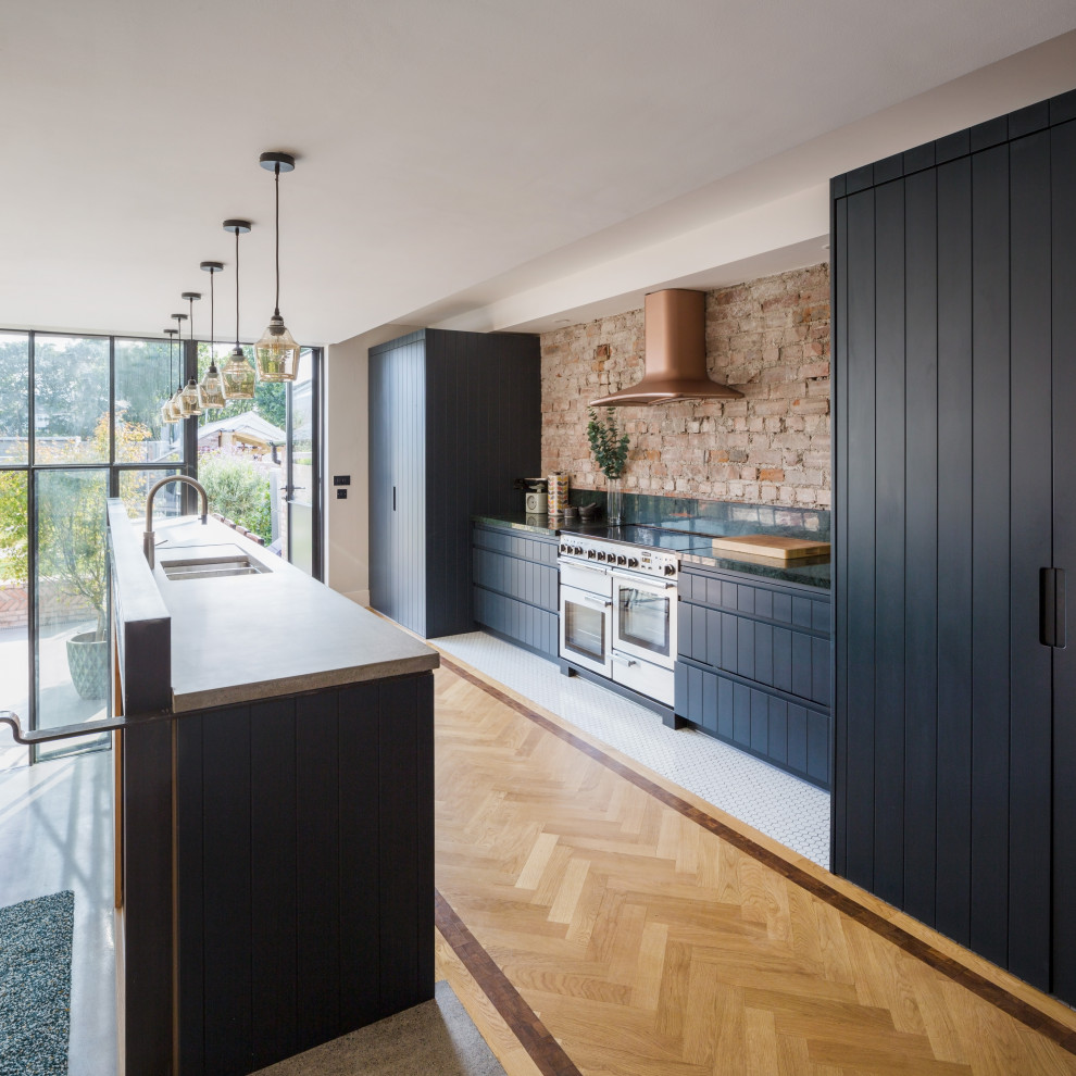 This is an example of a large contemporary galley kitchen in Dublin with a double-bowl sink, flat-panel cabinets, black cabinets, brown splashback, brick splashback, stainless steel appliances, with island, brown floor and black benchtop.