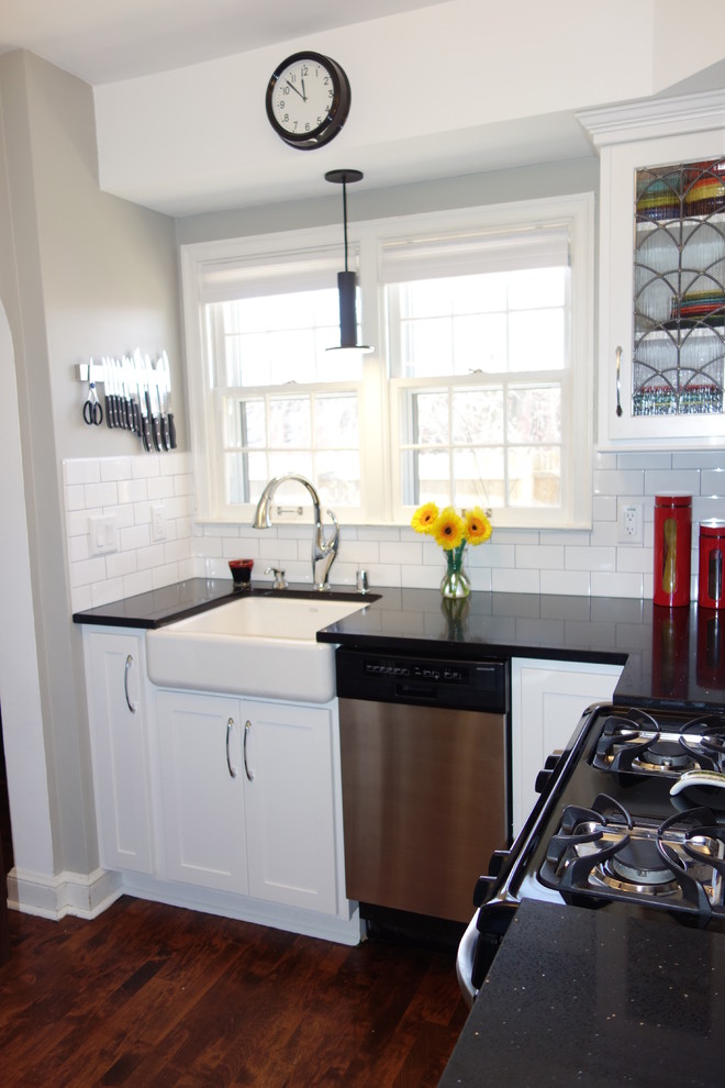 Enclosed kitchen - small transitional l-shaped dark wood floor and brown floor enclosed kitchen idea in Milwaukee with a farmhouse sink, shaker cabinets, white cabinets, quartz countertops, white backsplash, ceramic backsplash and stainless steel appliances