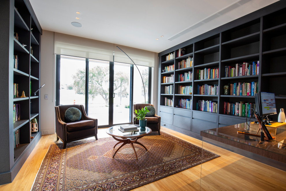 Foto di un ampio studio moderno con libreria, parquet chiaro, scrivania incassata e pavimento marrone