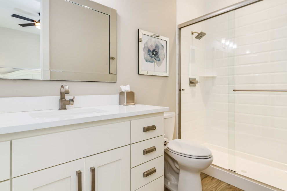 Mid-sized transitional 3/4 bathroom in Denver with shaker cabinets, white cabinets, an alcove shower, a two-piece toilet, white tile, porcelain tile, brown walls, medium hardwood floors, an undermount sink, engineered quartz benchtops, brown floor, a sliding shower screen and white benchtops.