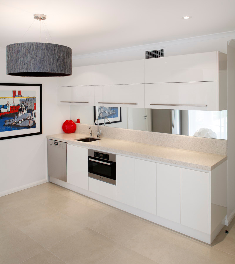 Inspiration for a small contemporary galley open plan kitchen in Sydney with an undermount sink, flat-panel cabinets, white cabinets, quartzite benchtops, white splashback, glass sheet splashback, stainless steel appliances, medium hardwood floors and with island.