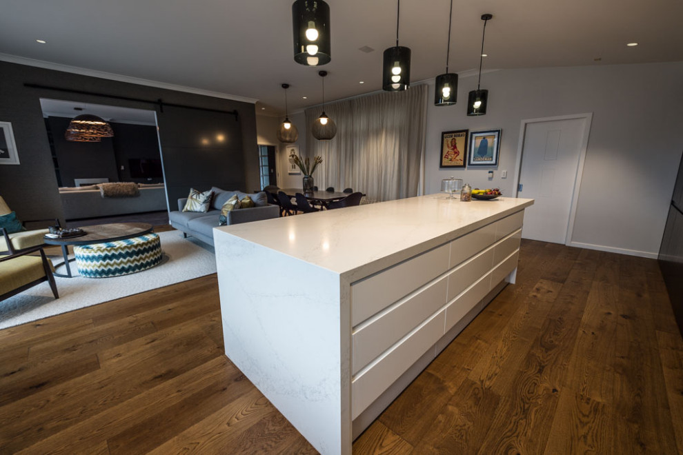 Transitional galley open plan kitchen in Wellington with white cabinets, marble benchtops, white splashback, marble splashback, stainless steel appliances, medium hardwood floors, with island, brown floor and white benchtop.