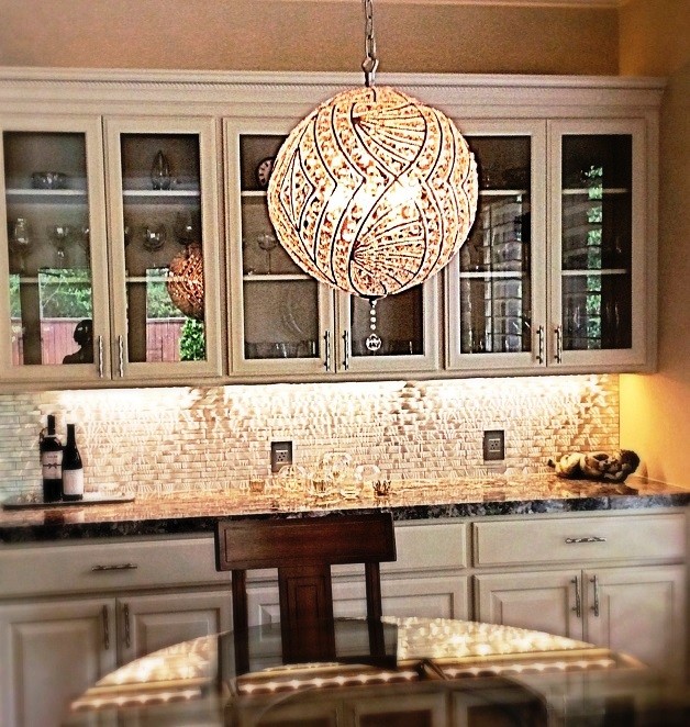 Inspiration for a mid-sized transitional l-shaped travertine floor eat-in kitchen remodel in Houston with a farmhouse sink, raised-panel cabinets, white cabinets, granite countertops, metallic backsplash, metal backsplash, stainless steel appliances and an island