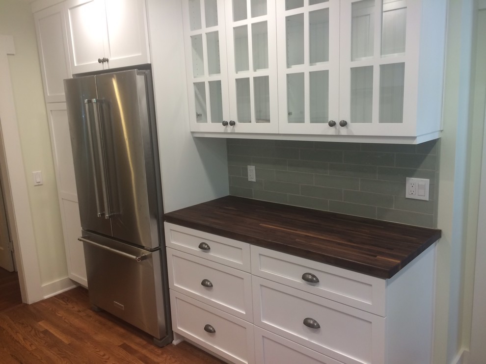Inspiration for a small arts and crafts galley kitchen in Los Angeles with a farmhouse sink, glass-front cabinets, white cabinets, wood benchtops, grey splashback, glass tile splashback, stainless steel appliances, medium hardwood floors and brown floor.
