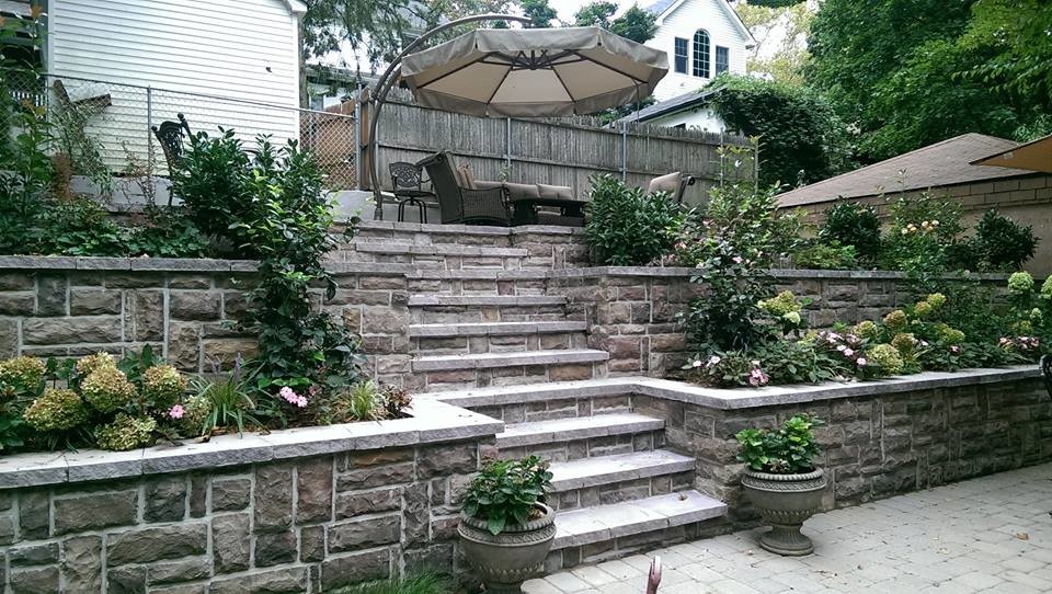 Large transitional sloped full sun formal garden in New York with a container garden and natural stone pavers for summer.