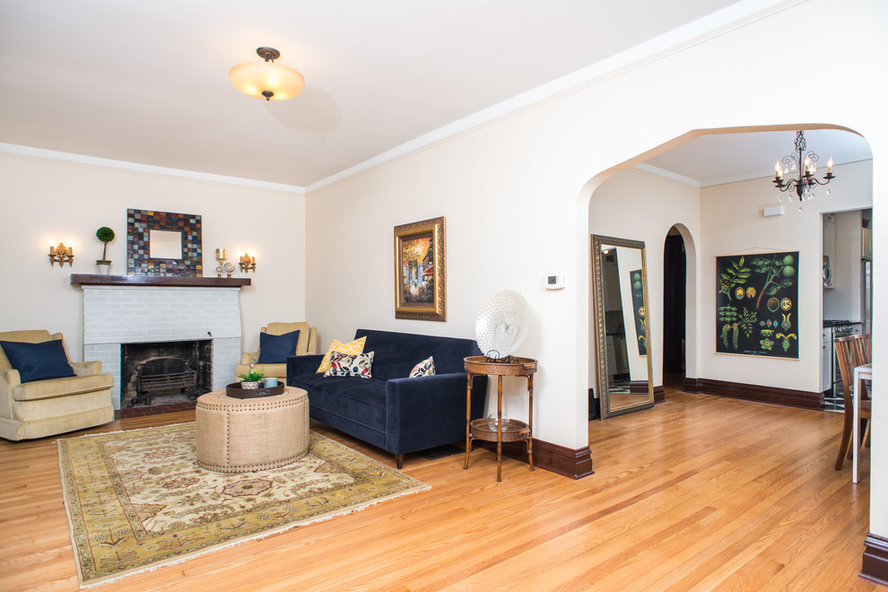 This is an example of a mid-sized traditional living room in Detroit with white walls, light hardwood floors, a standard fireplace, a brick fireplace surround and no tv.
