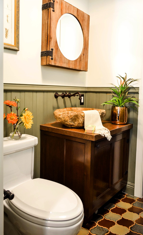 Small mediterranean powder room in Los Angeles with furniture-like cabinets, dark wood cabinets, a one-piece toilet, green tile, white walls, ceramic floors, a vessel sink, copper benchtops, multi-coloured floor and brown benchtops.