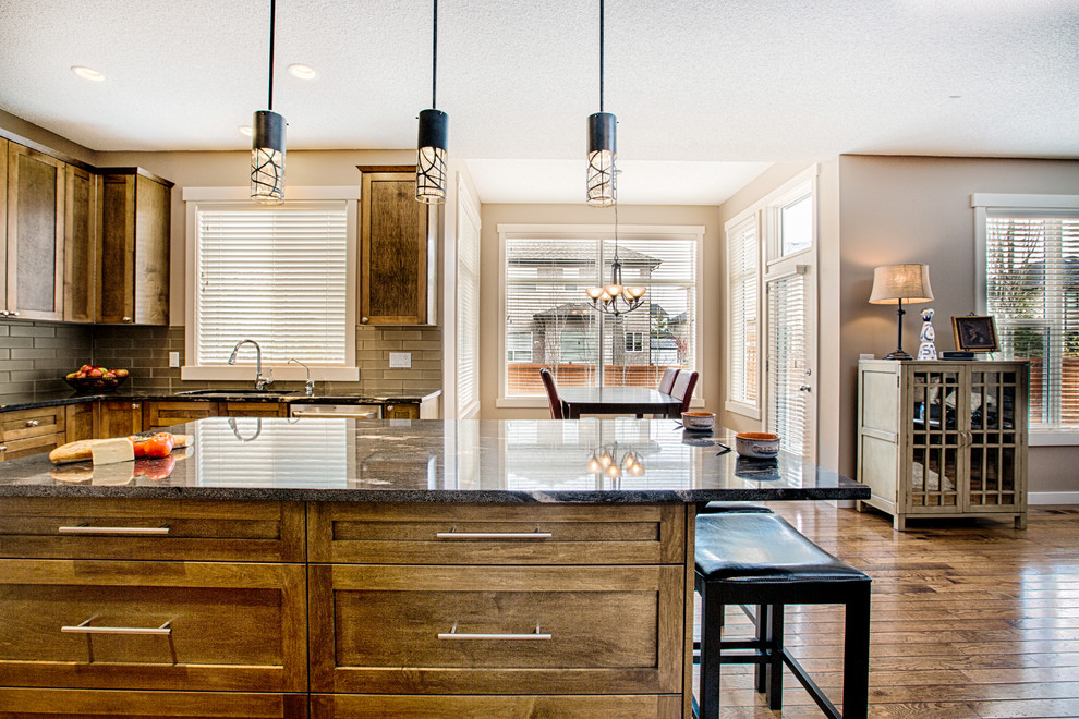 Inspiration for a mid-sized rustic u-shaped medium tone wood floor and brown floor eat-in kitchen remodel in Calgary with an undermount sink, shaker cabinets, medium tone wood cabinets, granite countertops, gray backsplash, glass tile backsplash, stainless steel appliances and an island