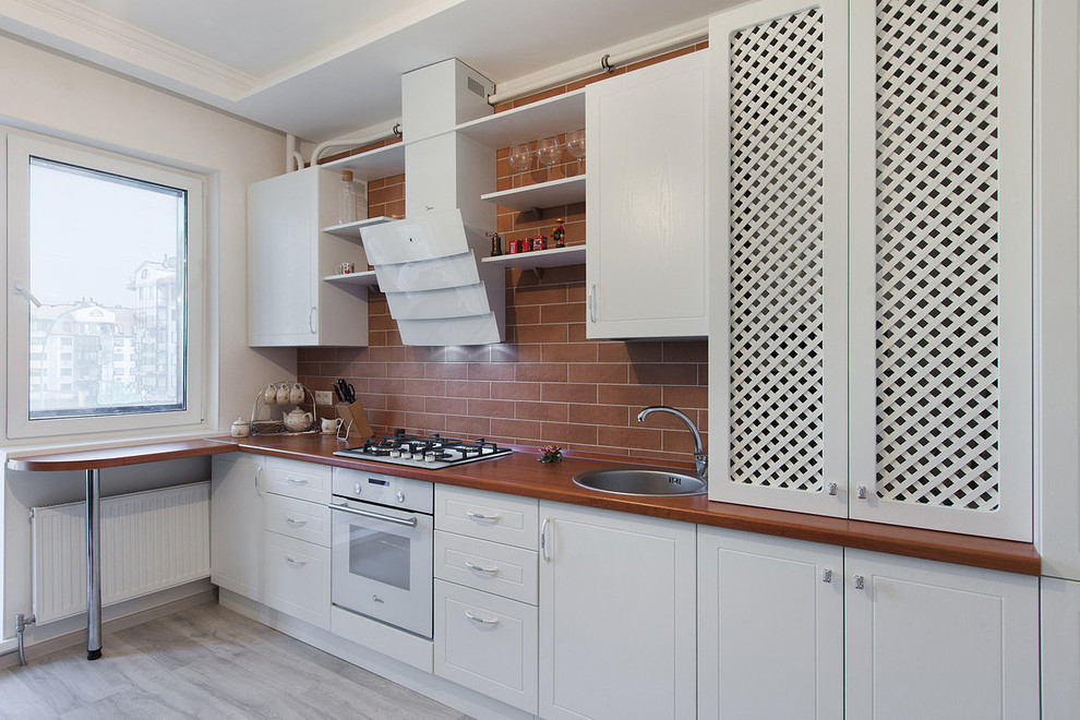 Photo of a transitional single-wall kitchen in Moscow with a drop-in sink, white cabinets, brown splashback, white appliances, brown benchtop, wood benchtops, subway tile splashback and a peninsula.