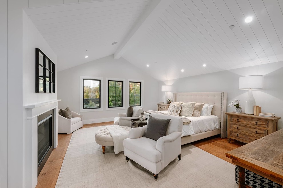 Inspiration for a mid-sized country master bedroom in Los Angeles with white walls, light hardwood floors, a standard fireplace, a wood fireplace surround and brown floor.