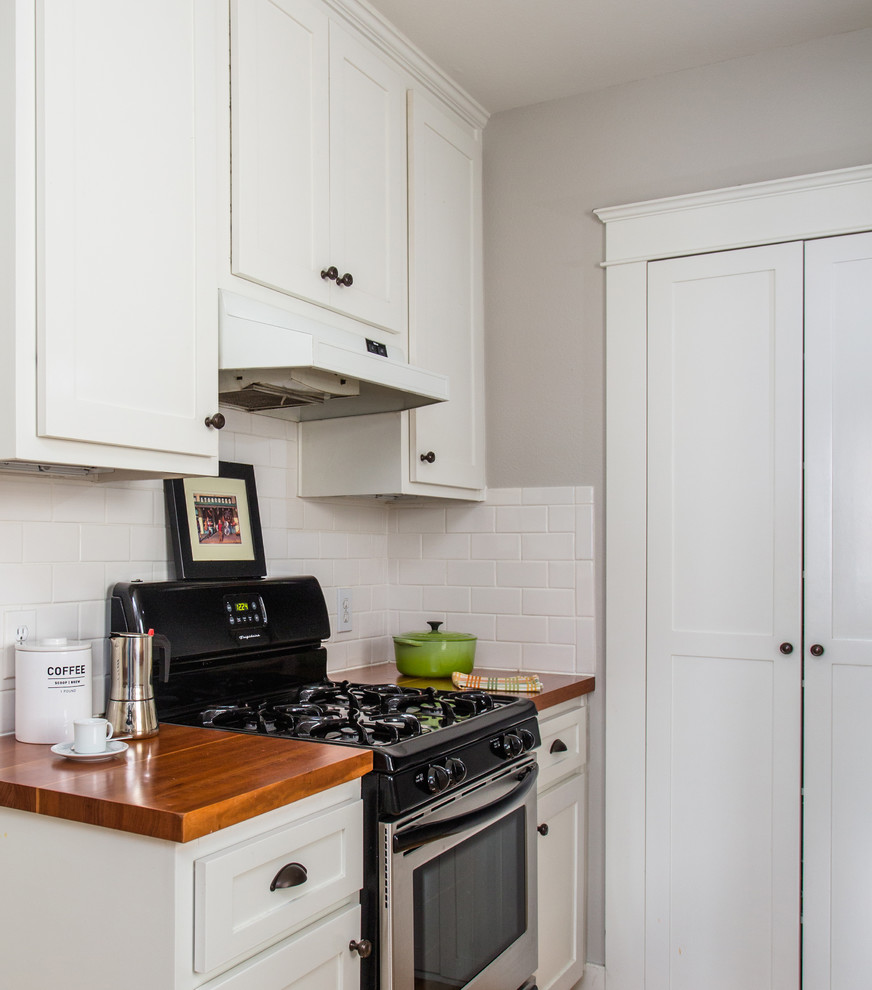 Mid-sized transitional galley medium tone wood floor enclosed kitchen photo in Santa Barbara with a drop-in sink, shaker cabinets, white cabinets, white backsplash, ceramic backsplash and stainless steel appliances