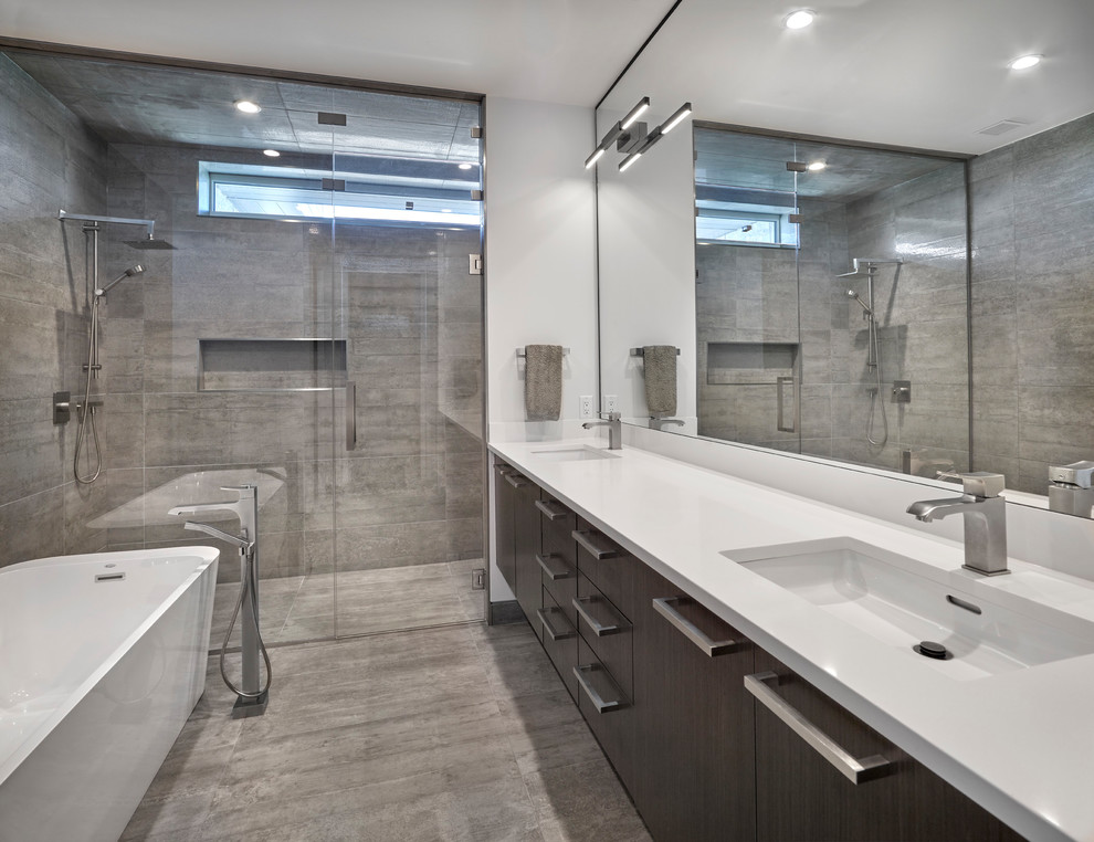 This is an example of a large contemporary master bathroom in Edmonton with flat-panel cabinets, dark wood cabinets, a freestanding tub, a one-piece toilet, gray tile, white walls, an undermount sink, grey floor, a hinged shower door, an alcove shower, cement tile, cement tiles and solid surface benchtops.