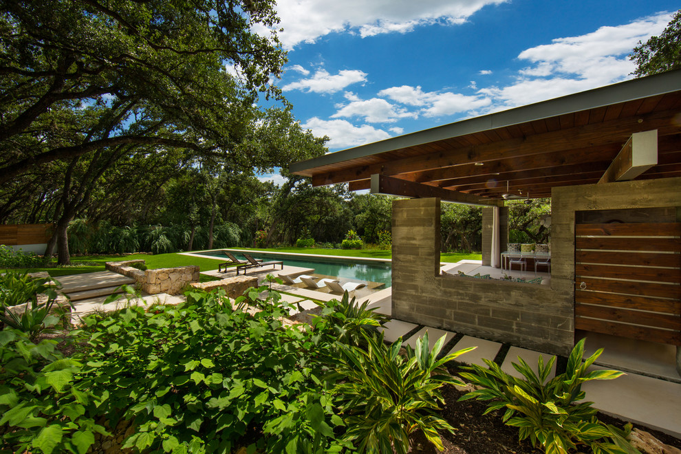 This is an example of a large modern backyard rectangular lap pool in Austin with a pool house and natural stone pavers.
