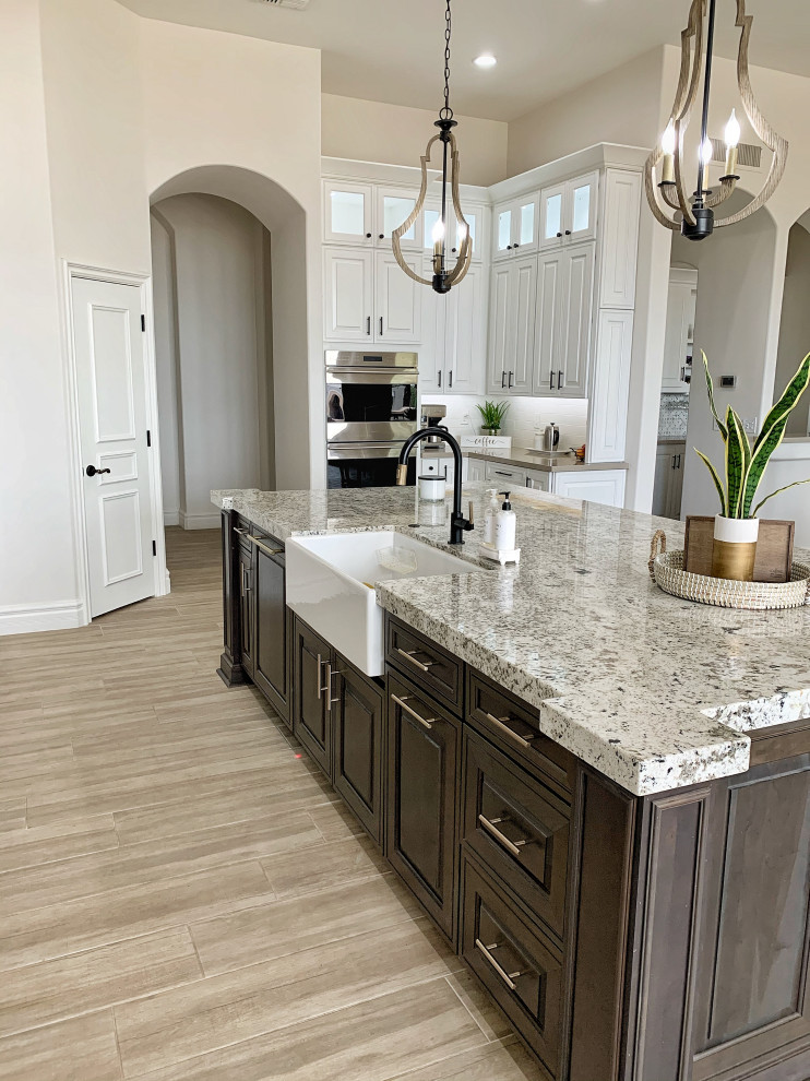 Photo of a large transitional l-shaped open plan kitchen in Phoenix with a farmhouse sink, raised-panel cabinets, white cabinets, quartz benchtops, white splashback, ceramic splashback, stainless steel appliances, cement tiles, with island, grey floor and beige benchtop.
