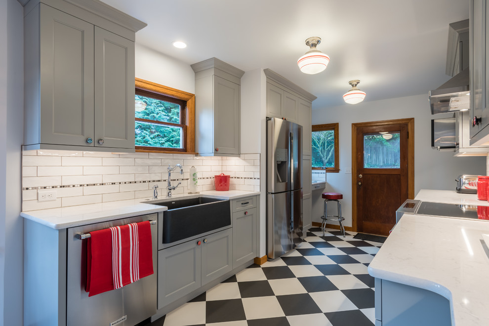 Photo of a mid-sized transitional galley kitchen in Seattle with a farmhouse sink, shaker cabinets, grey cabinets, quartz benchtops, multi-coloured splashback, porcelain splashback, stainless steel appliances, vinyl floors, no island, multi-coloured floor and white benchtop.
