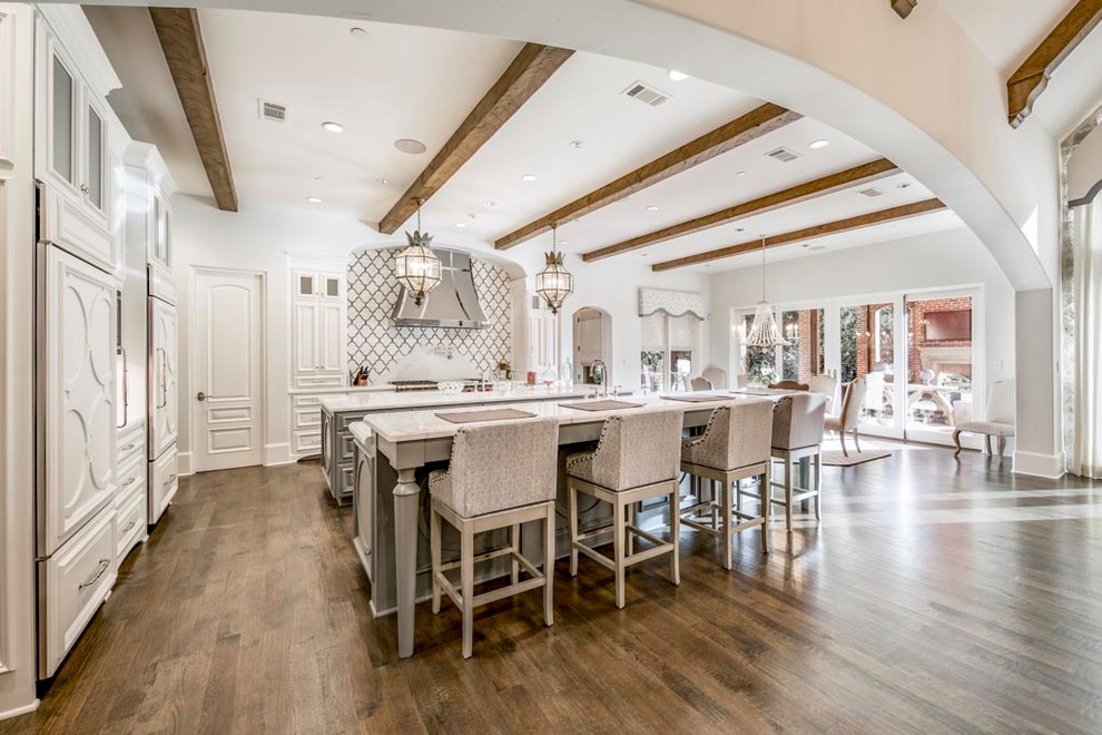 This is an example of an expansive transitional l-shaped eat-in kitchen in Dallas with raised-panel cabinets, white cabinets, marble benchtops, multi-coloured splashback, stainless steel appliances, multiple islands, dark hardwood floors, brown floor, a farmhouse sink and stone tile splashback.