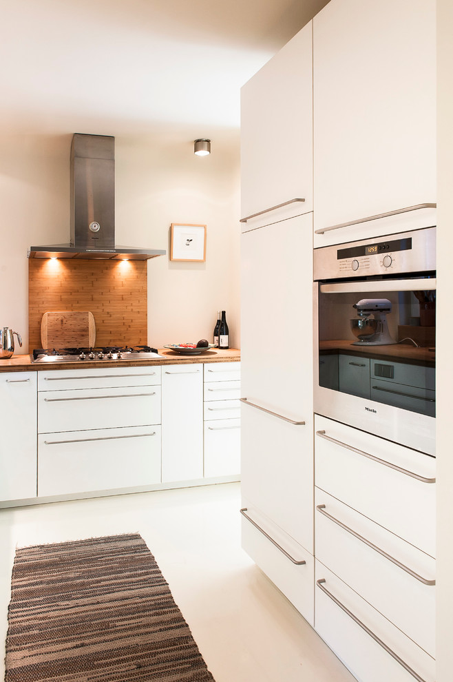Design ideas for a mid-sized eclectic open plan kitchen in Hamburg with a double-bowl sink, flat-panel cabinets, white cabinets, stainless steel appliances, concrete floors, no island, wood benchtops, brown splashback and matchstick tile splashback.