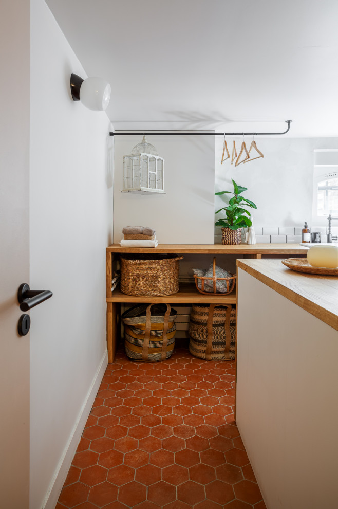 Photo of a mid-sized mediterranean u-shaped dedicated laundry room in Paris with a farmhouse sink, white cabinets, wood benchtops, white splashback, subway tile splashback, white walls, terra-cotta floors and red floor.