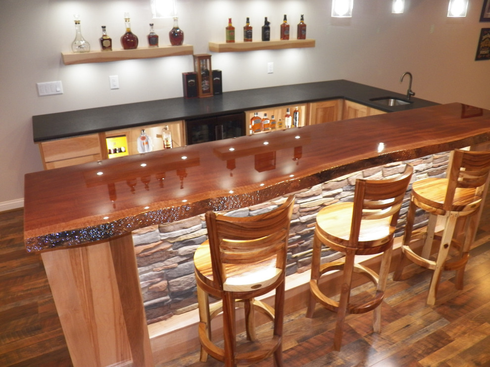 This is an example of a large rustic u-shaped wet bar in Cincinnati with a submerged sink, shaker cabinets, light wood cabinets, granite worktops, laminate floors, brown floors and black worktops.
