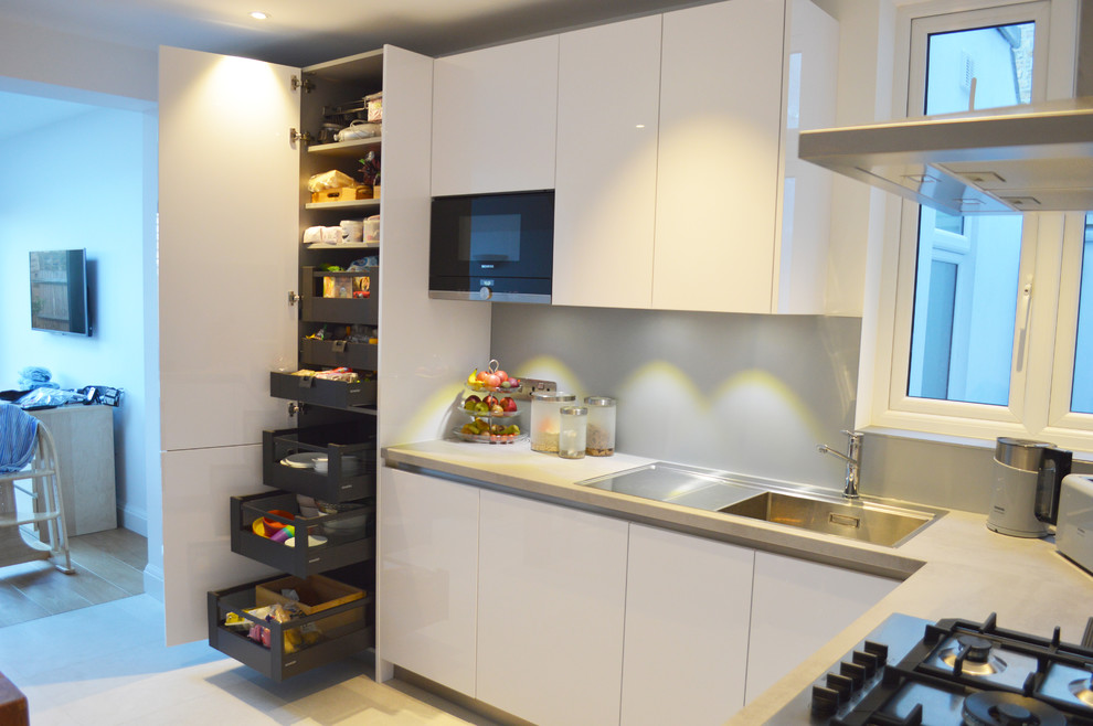 Photo of a mid-sized contemporary l-shaped eat-in kitchen in London with a drop-in sink, beaded inset cabinets, white cabinets, laminate benchtops, blue splashback, glass tile splashback, black appliances and no island.