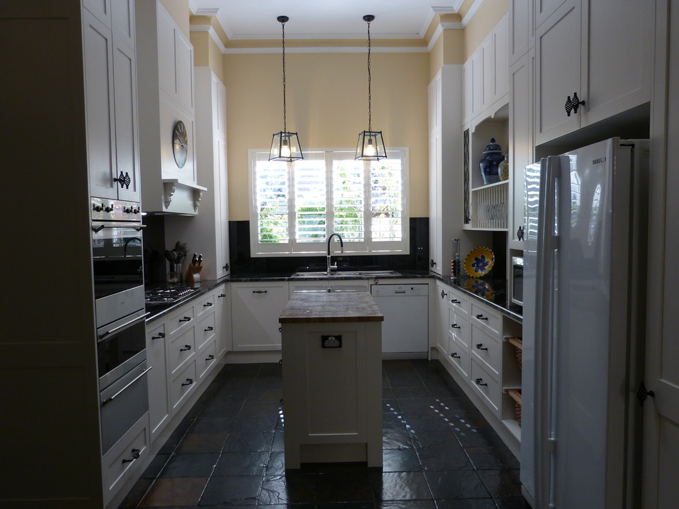 This is an example of a mid-sized traditional u-shaped separate kitchen in Adelaide with a double-bowl sink, shaker cabinets, white cabinets, granite benchtops, black splashback, glass tile splashback, white appliances, slate floors, with island, black floor and black benchtop.