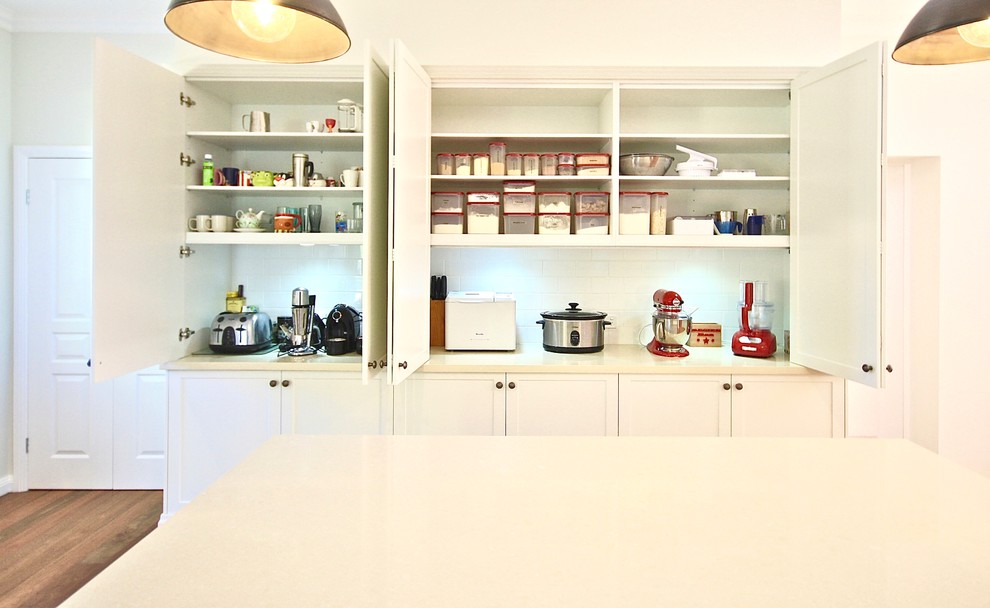 Photo of a mid-sized transitional u-shaped eat-in kitchen in Sydney with a farmhouse sink, shaker cabinets, white cabinets, quartz benchtops, white splashback, porcelain splashback, black appliances, medium hardwood floors and with island.