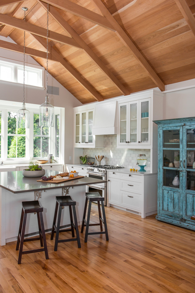 This is an example of a large beach style u-shaped kitchen in Boston with a farmhouse sink, shaker cabinets, quartz benchtops, white splashback, subway tile splashback, medium hardwood floors, with island and white cabinets.