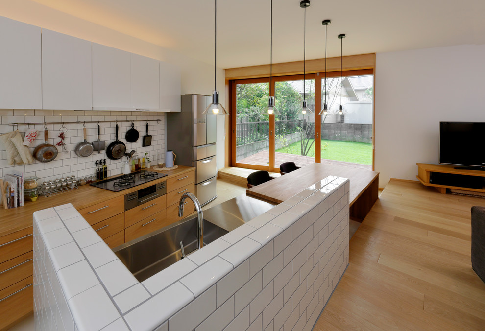 Design ideas for an asian galley open plan kitchen in Other with an integrated sink, flat-panel cabinets, white cabinets, wood benchtops, white splashback, light hardwood floors, a peninsula, beige floor and brown benchtop.