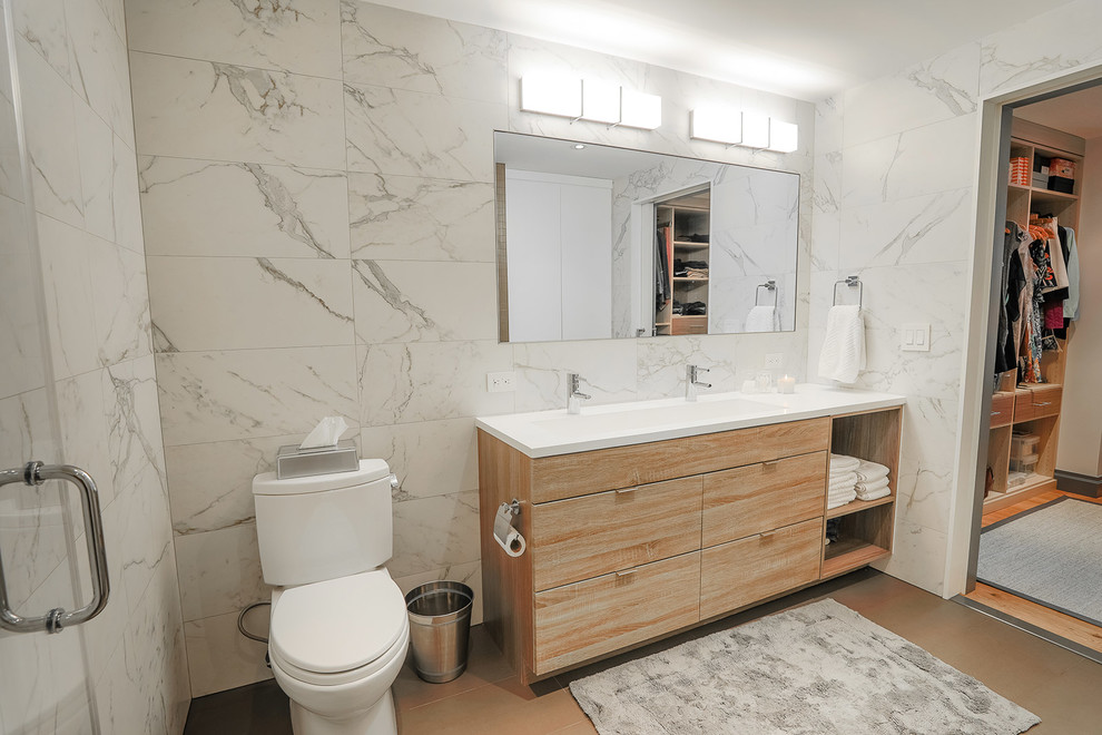 Photo of a large contemporary master bathroom in New York with flat-panel cabinets, light wood cabinets, an alcove shower, a two-piece toilet, gray tile, white tile, porcelain tile, grey walls, porcelain floors, a trough sink, brown floor and a hinged shower door.
