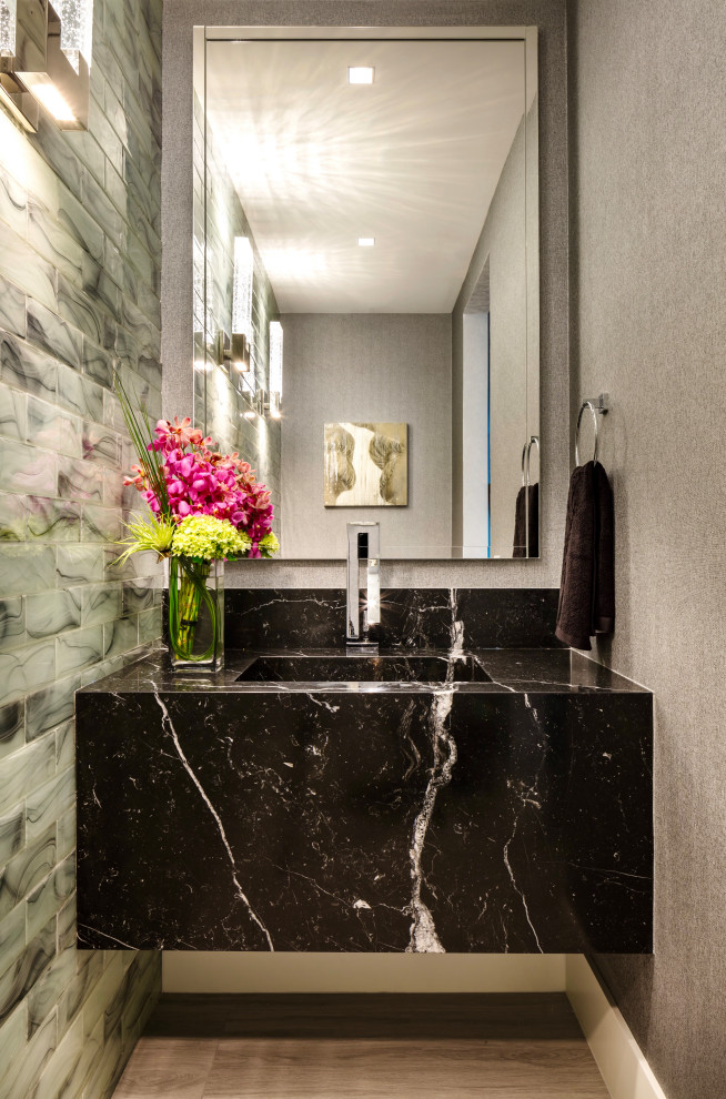 This is an example of a small contemporary powder room with black cabinets, a one-piece toilet, white tile, glass tile, grey walls, light hardwood floors, an integrated sink, marble benchtops, grey floor, black benchtops, a floating vanity, coffered and wallpaper.