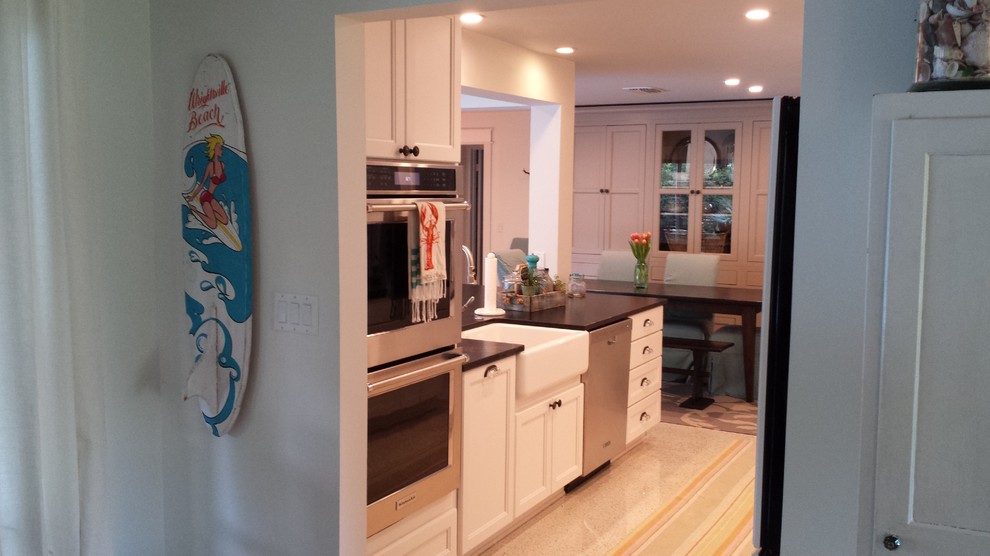 Kitchen - transitional galley kitchen idea in Tampa with a farmhouse sink, recessed-panel cabinets, white cabinets, granite countertops, beige backsplash, glass tile backsplash, paneled appliances and black countertops